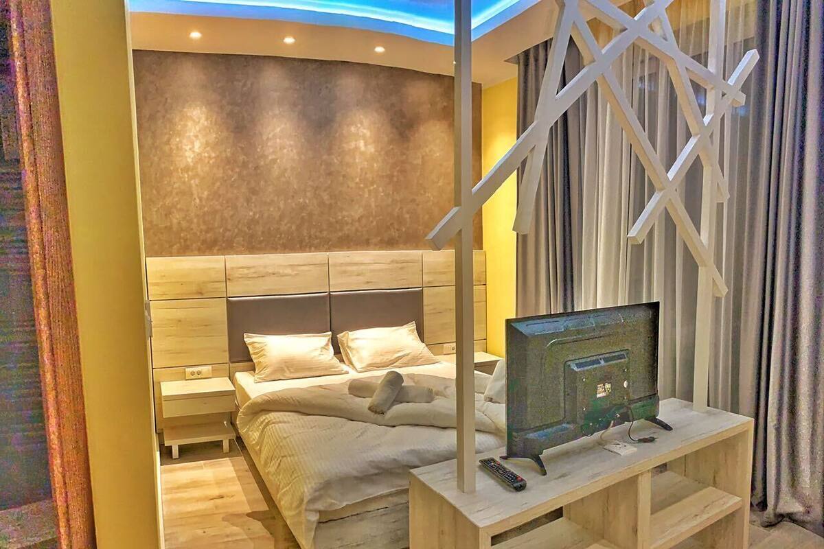 A modern bedroom with a wooden bed, a TV on a wooden stand, and a nightstand.