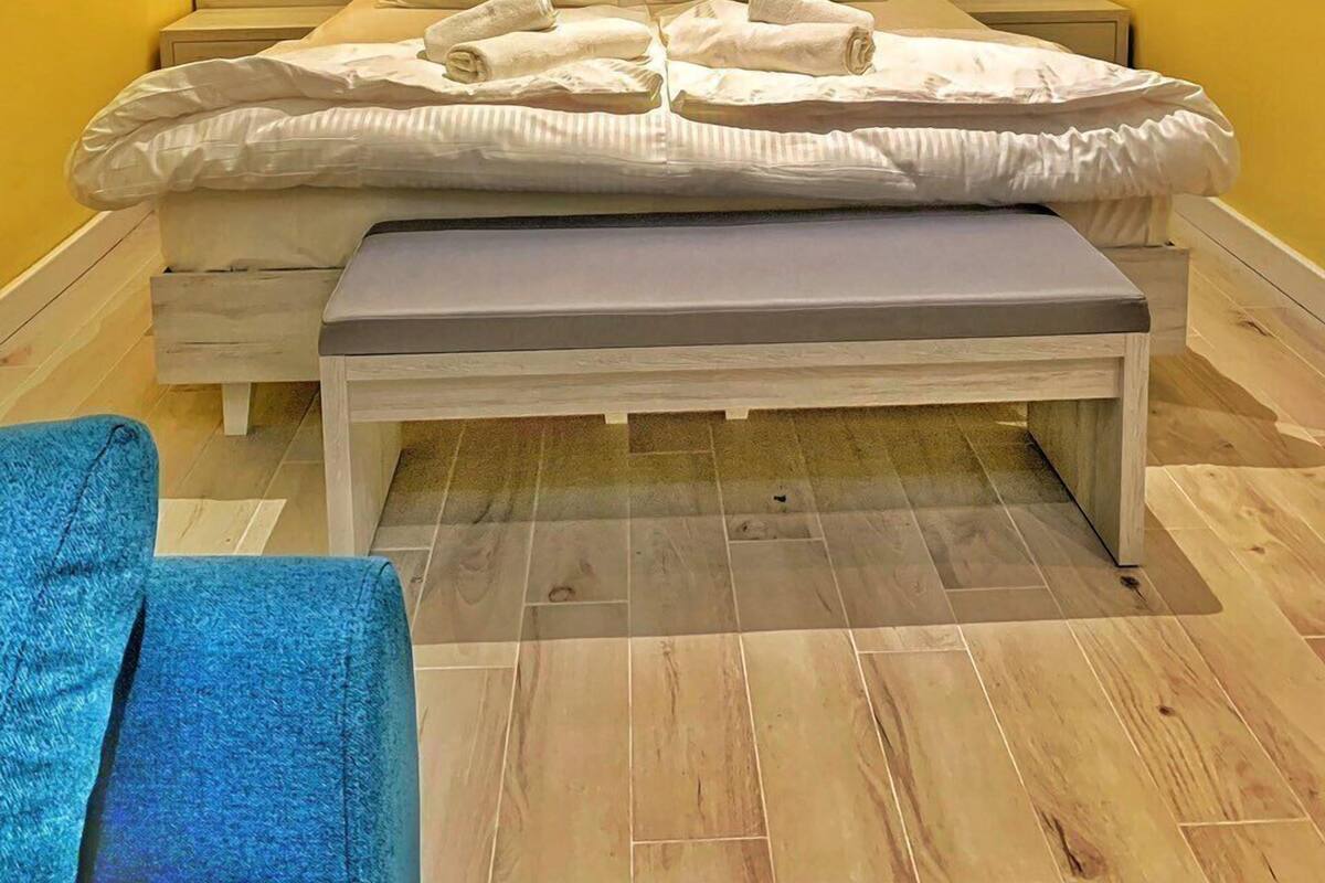 A bedroom with a wooden headboard, two bedside lamps, a bed with white bedding, a bench, and a blue towel on the floor.