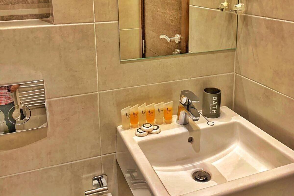 A bathroom with a large mirror, a sink, and a hairdryer mounted on the wall.