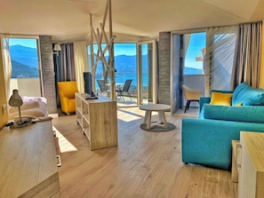 A modern living room with a wooden floor, a blue sofa, a yellow chair, and a small round table. - Hotel Pierina (Budva)