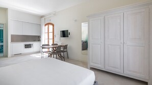 Quarto de hotel moderno com uma cama grande, área de refeições com mesa e cadeiras, cozinha e guarda-roupa.