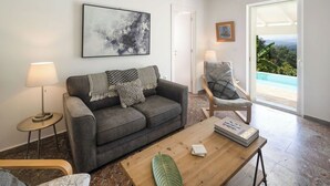A living room with a sofa, a chair, a coffee table, a lamp, and a painting on the wall. - PRESTIGE VILLAS 'Tree Tops' - North East Coast Villa with infinity pool... (Agios Markos, Corfu)