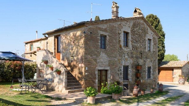 A stone building with a staircase leading to the entrance, outdoor seating, and potted plants. - Ancient farm la Martinella Depandance apartment (Siena)