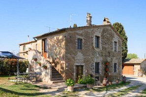Traditional stone building with a symmetrical facade and central entrance, featuring a small staircase and well-manicured grounds.