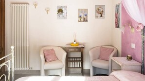 A bedroom with two chairs, a bedside table with a lamp, a radiator, and wall-mounted artwork. - Ancient farm la Martinella Depandance apartment (Siena)
