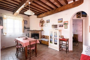 A cozy room with a wooden ceiling, a fireplace, a dining table with chairs, and a cabinet with glass doors.