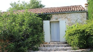 A stone building with a tiled roof, a wooden door, and a small set of stone steps leading to the entrance. - Old stone sheepfold of 129m2 and its private garden (Forcalquier)
