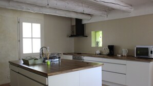 A kitchen with a wooden countertop, white cabinets, a stove, a microwave, and a window. - Old stone sheepfold of 129m2 and its private garden (Forcalquier)