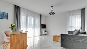 Un salon moderne avec une table à manger en bois, un canapé gris et un téléviseur posé sur un meuble blanc.