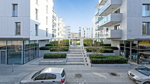 Un immeuble d’appartements moderne doté d’un escalier central, de balcons en verre et d’une petite cour intérieure agrémentée de verdure.