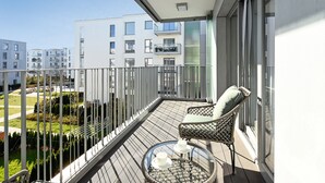 Un balcon doté d'une balustrade en verre, de meubles en osier et offrant une vue sur les bâtiments voisins.