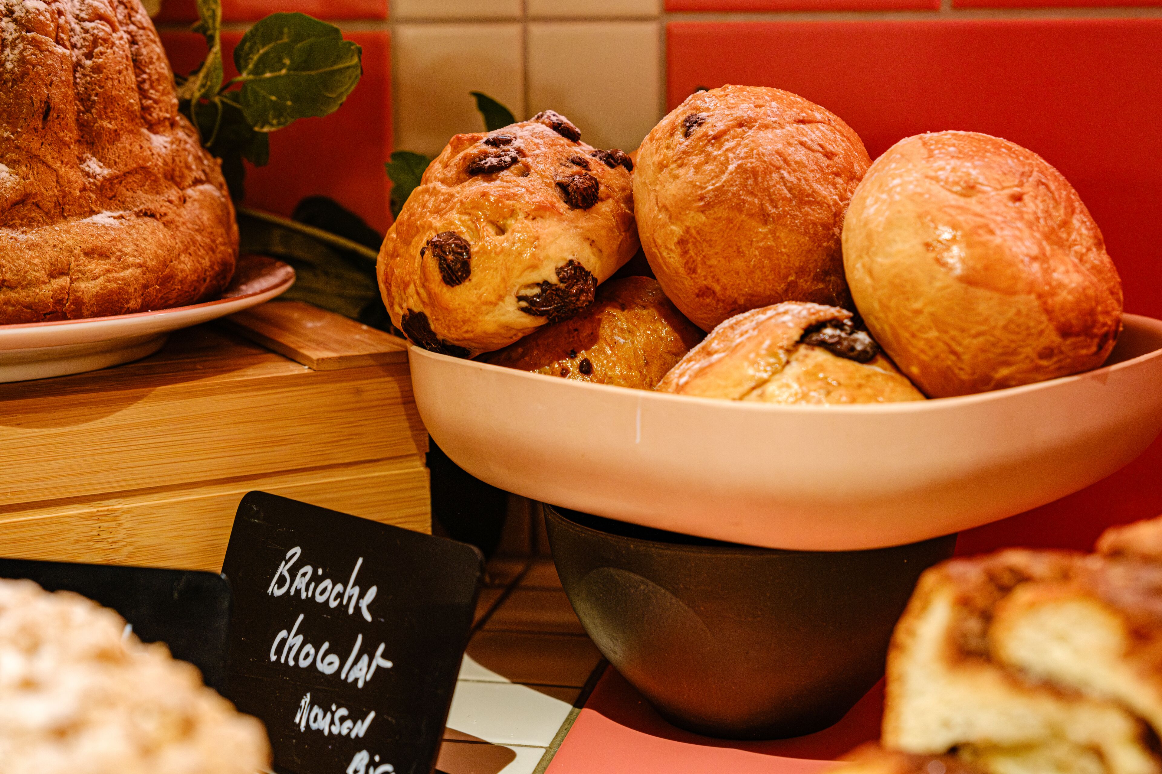Una presentación de varios productos horneados, incluyendo muffins de brioche con chocolate y otras pastelerías, dispuestas sobre una mesa con un cartel que indica el tipo de comida.
