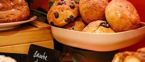 Esposizione di dolci appena sfornati, tra cui brioche, muffin al cioccolato e altri pasticcini, disposti su un tavolo con un cartello che indica il tipo di cibo.