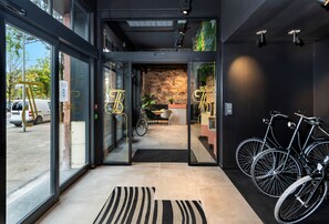 Entrada moderna de un hotel con puertas de cristal, alfombra blanco y negro y bicicletas estacionadas en el interior.