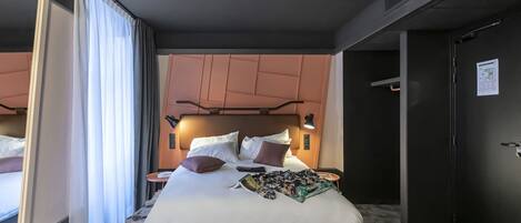 Moderni hotellihuone, jossa on suuri sänky, sängynpääty, jossa on integroitu valaistus, pieni yöpöytä ja ovi, jossa on kartta.
