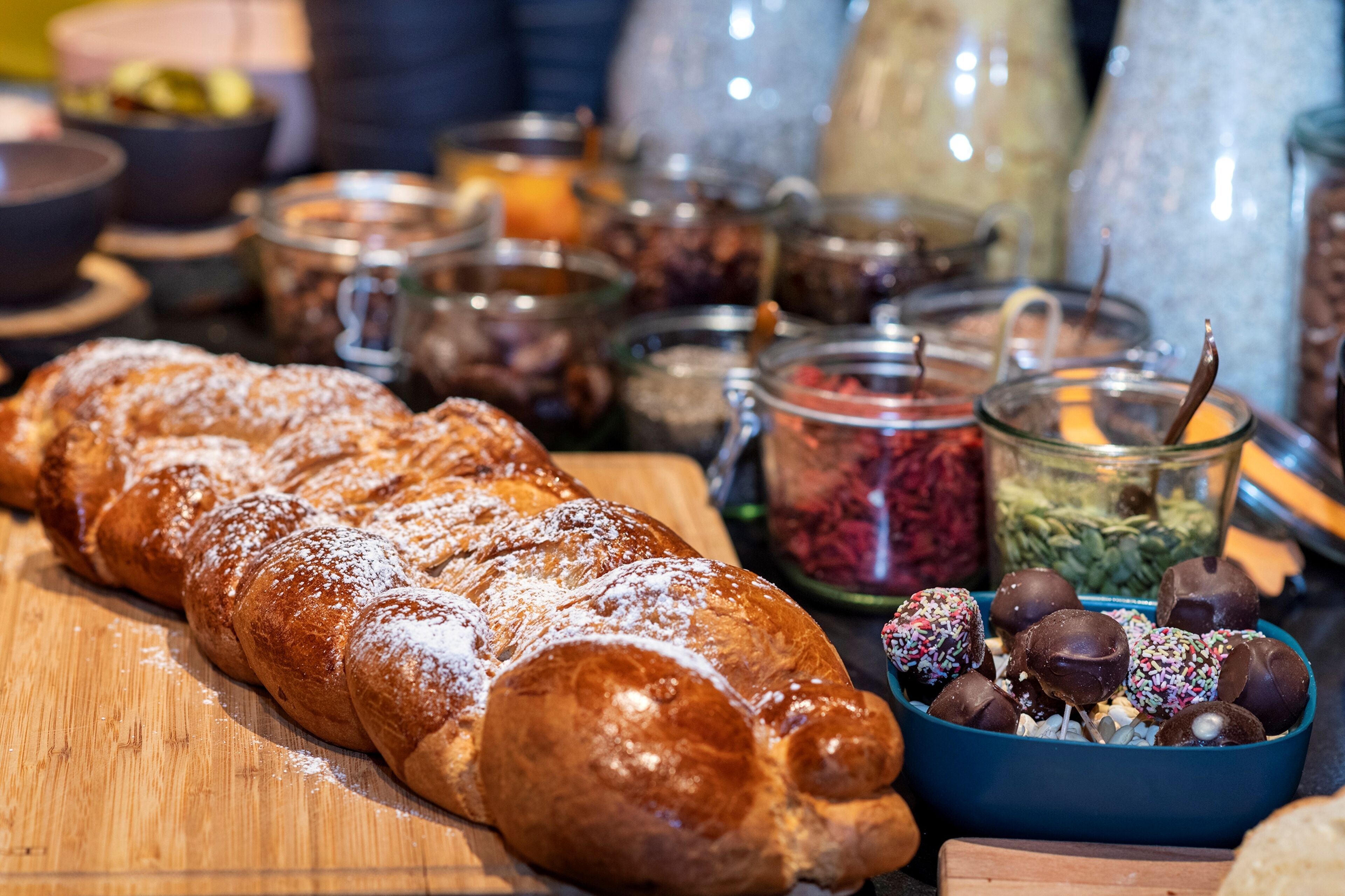 Une variété d’aliments, notamment des pâtisseries et des confiseries enrobées de chocolat, sont disposés sur une table en bois.