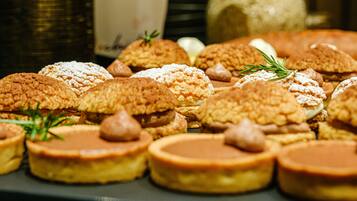 Une variété de pâtisseries disposées sur une assiette, comprenant des motifs ronds et croisés, certaines saupoudrées de sucre glace et décorées de brins de romarin.