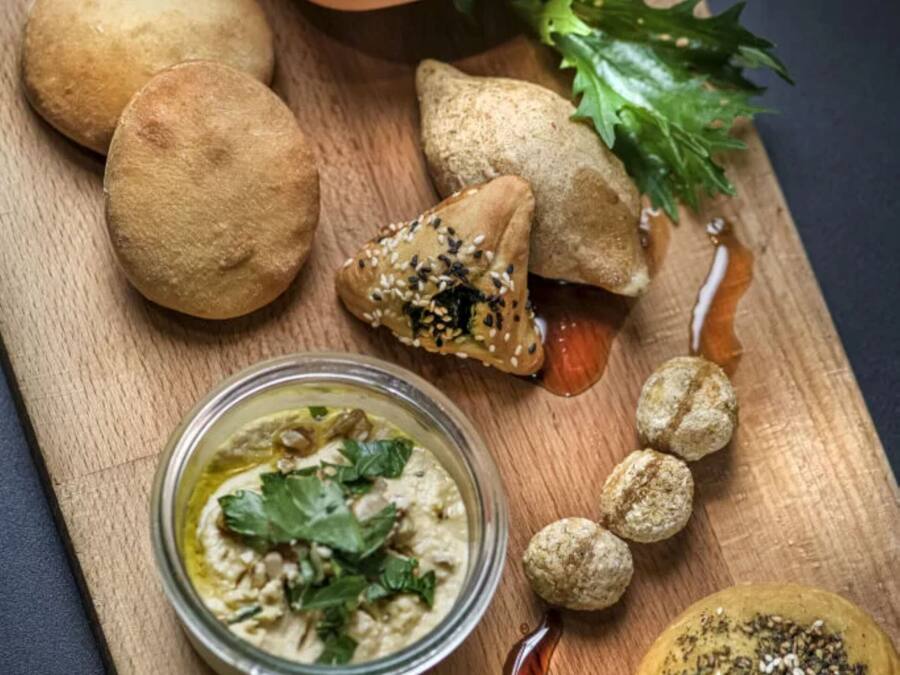 A wooden board with various food items including bread, hummus, and a salad.
