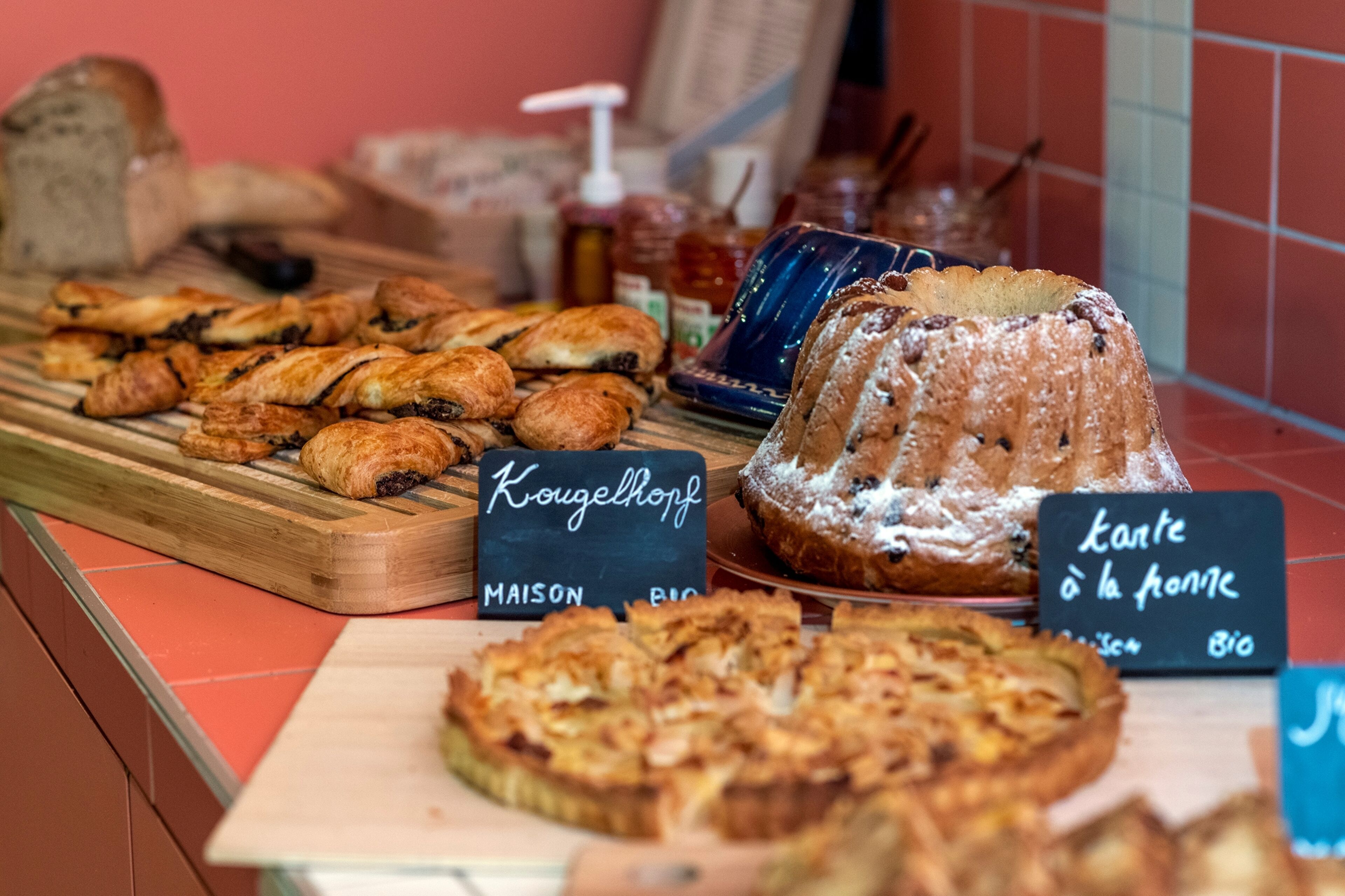 Une variété de produits de boulangerie sont exposés, notamment un kougelhopf et une tarte, et des panneaux indiquent qu’ils sont préparés avec des ingrédients biologiques.