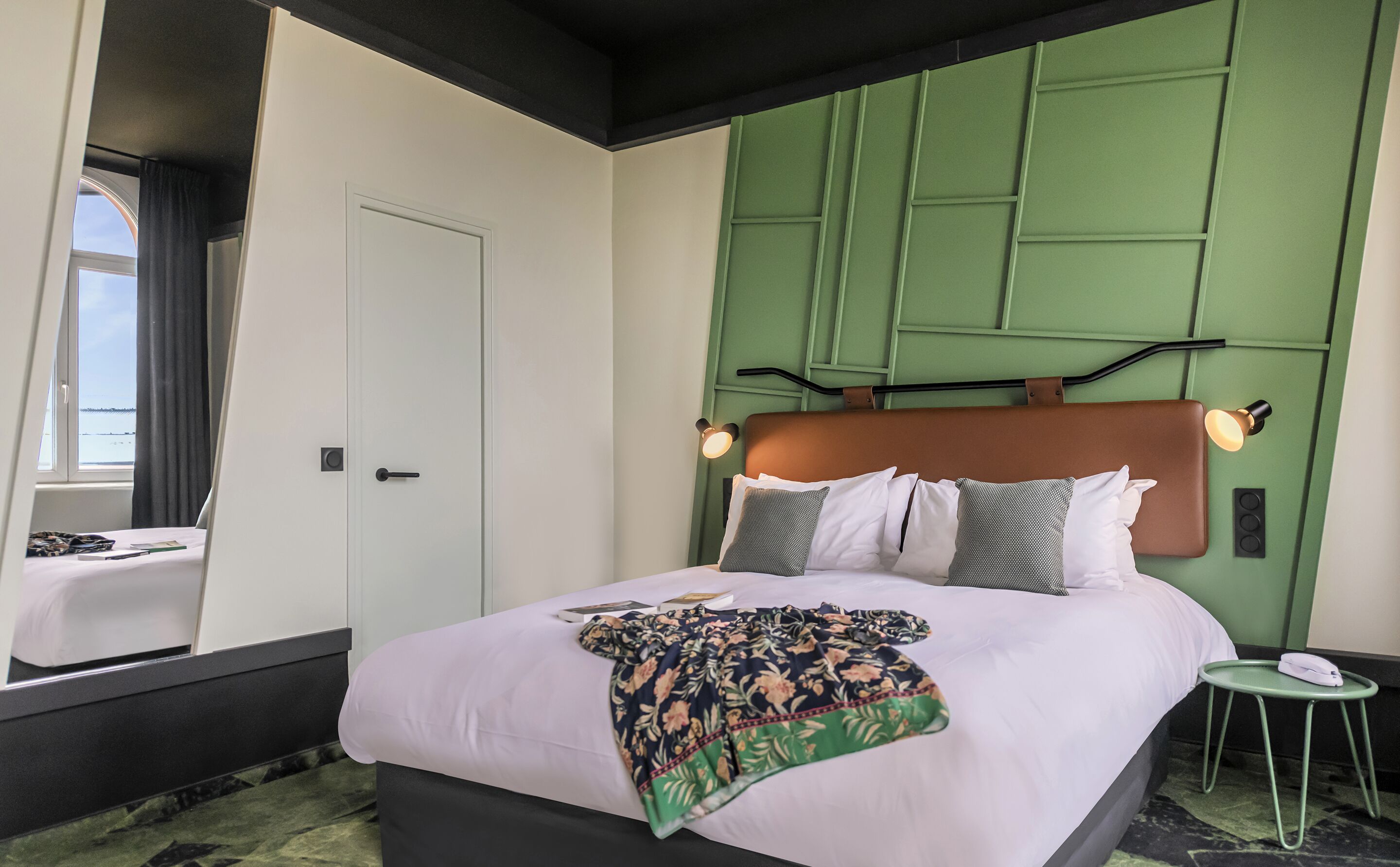 Habitación de hotel con una cama grande, una pared de acento verde, una mesita de noche pequeña y una ventana con cortinas.