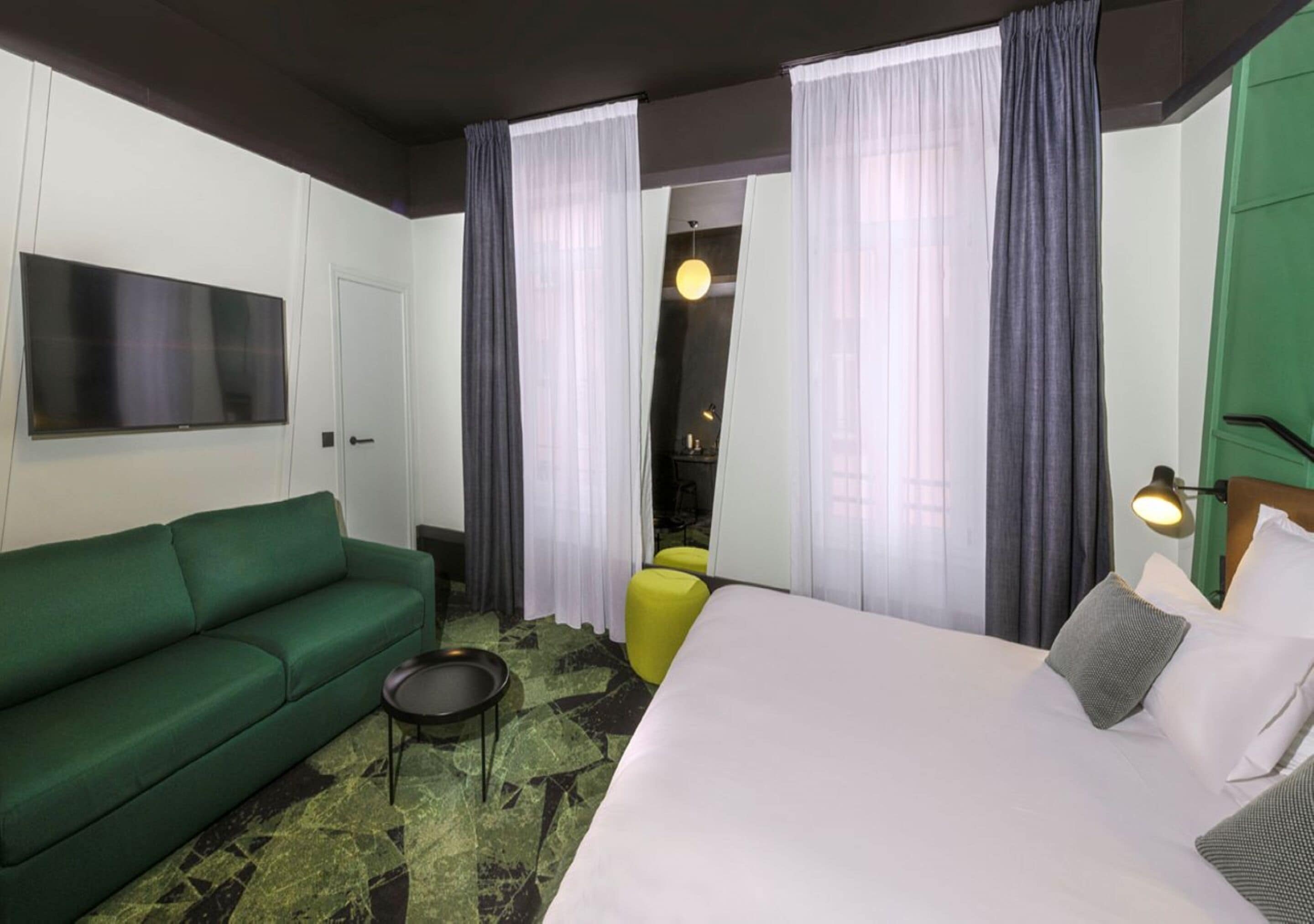 A hotel room with a green sofa, a bed with white bedding, a small round table, and a yellow chair.