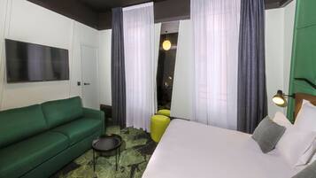 A hotel room with a green sofa, a bed with white bedding, a small round table, and a yellow chair.