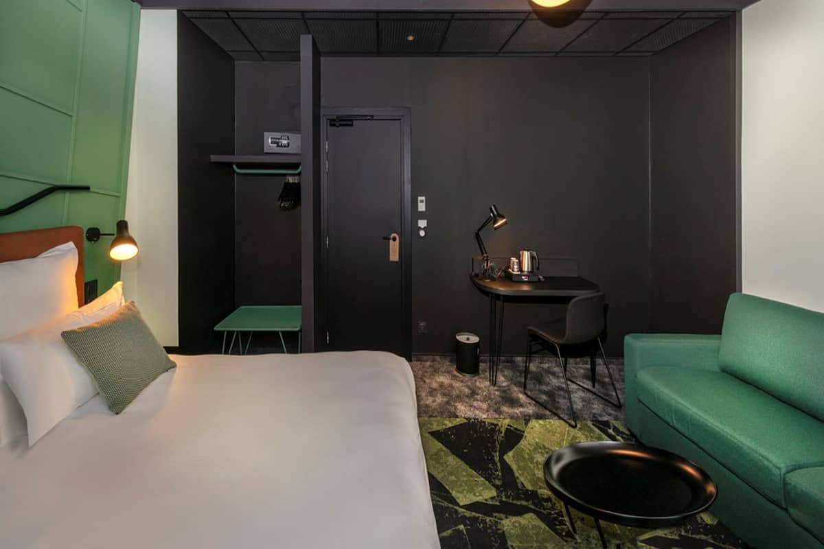 A hotel room with a bed, a green sofa, a desk with a lamp, and a small table.