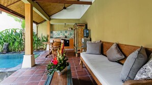 Area relax esterna coperta con piscina, tavolo da pranzo e cucina sullo sfondo.