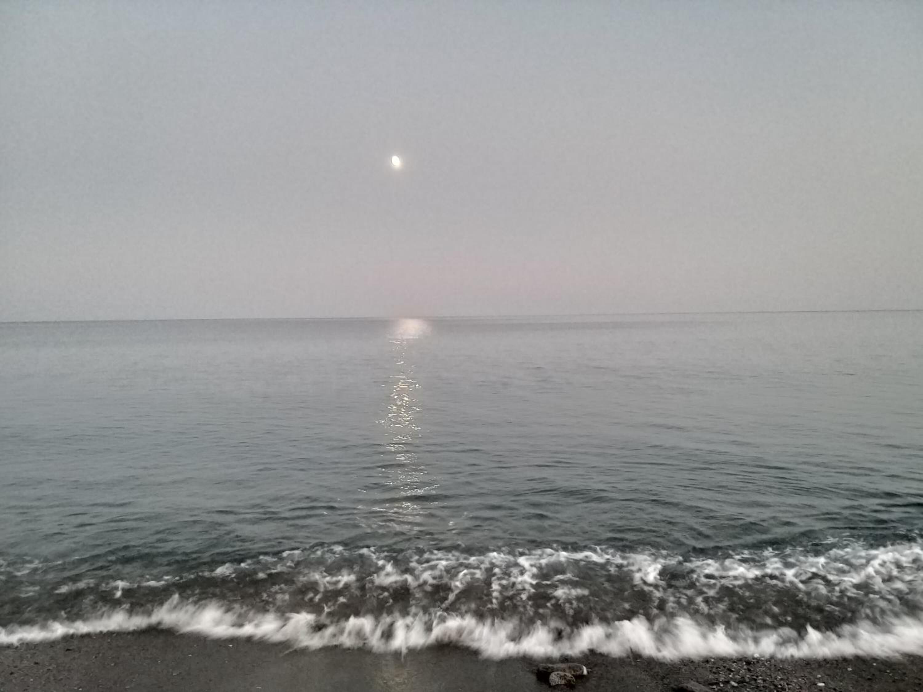 A calm sea with gentle waves and a visible moon reflection on the water.