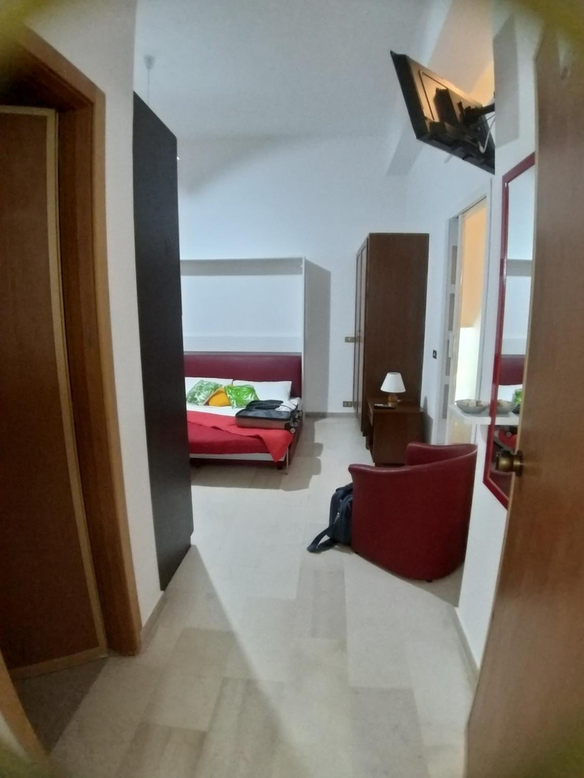A narrow hallway leading to a bedroom with a bed, a desk, and a chair.