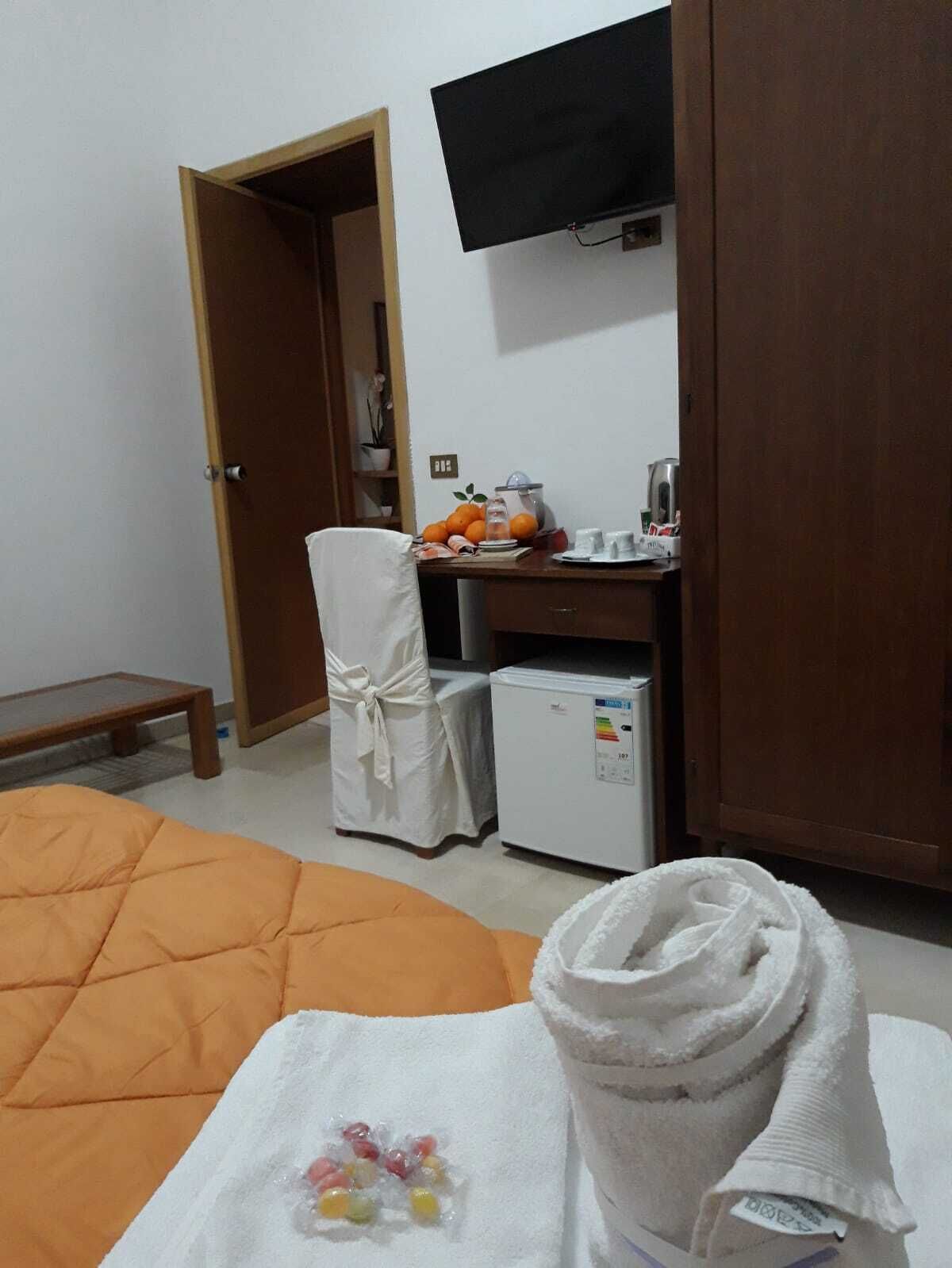 A hotel room with a bed, a small desk with a refrigerator, a television mounted on the wall, and a door leading to another room.