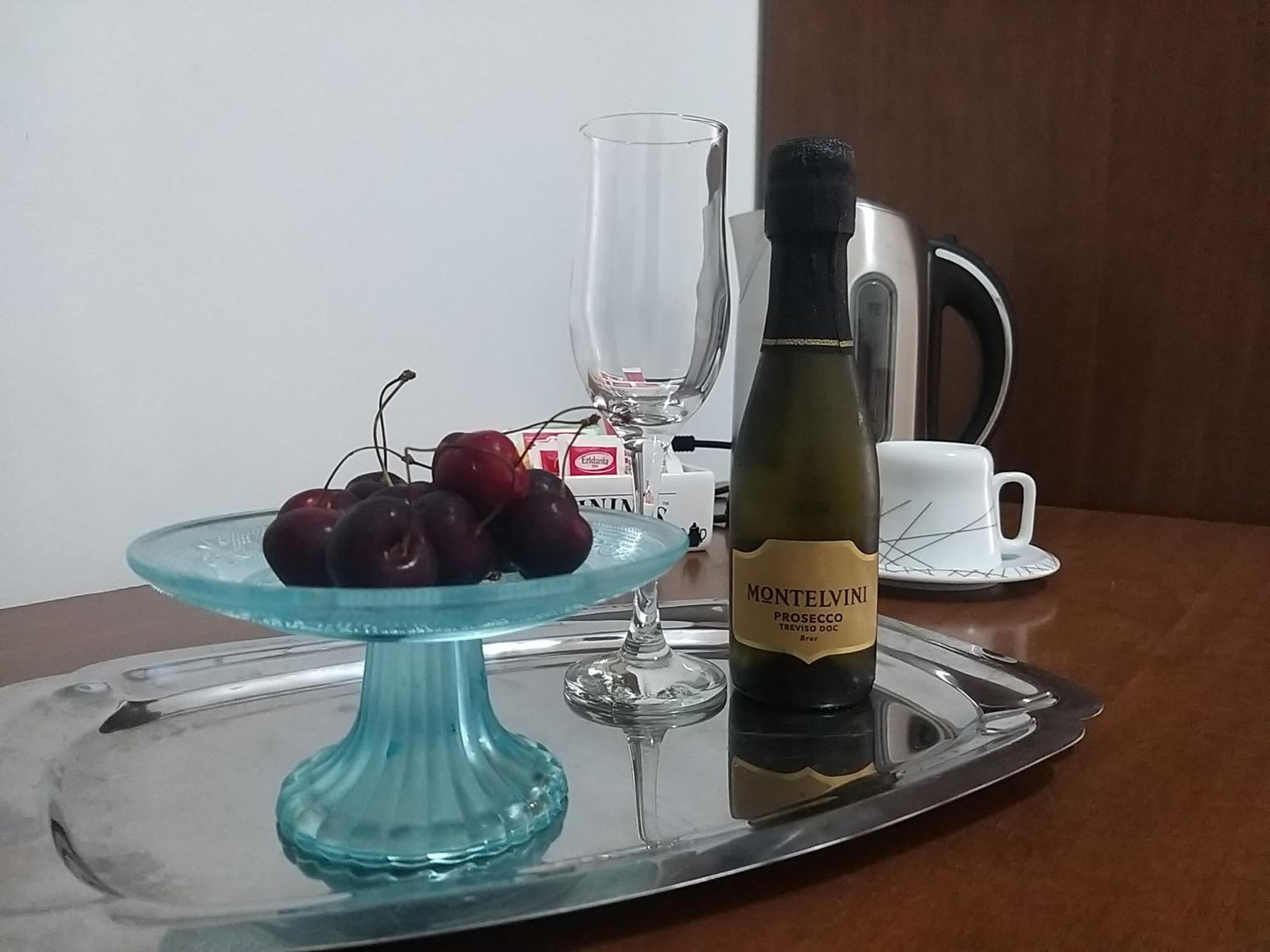 Ein Esstisch mit einer klaren Weinflasche, einem blauen Glas-Kuchenständchen mit Kirschen, einem Weinglas und einer weißen Kaffeetasse.