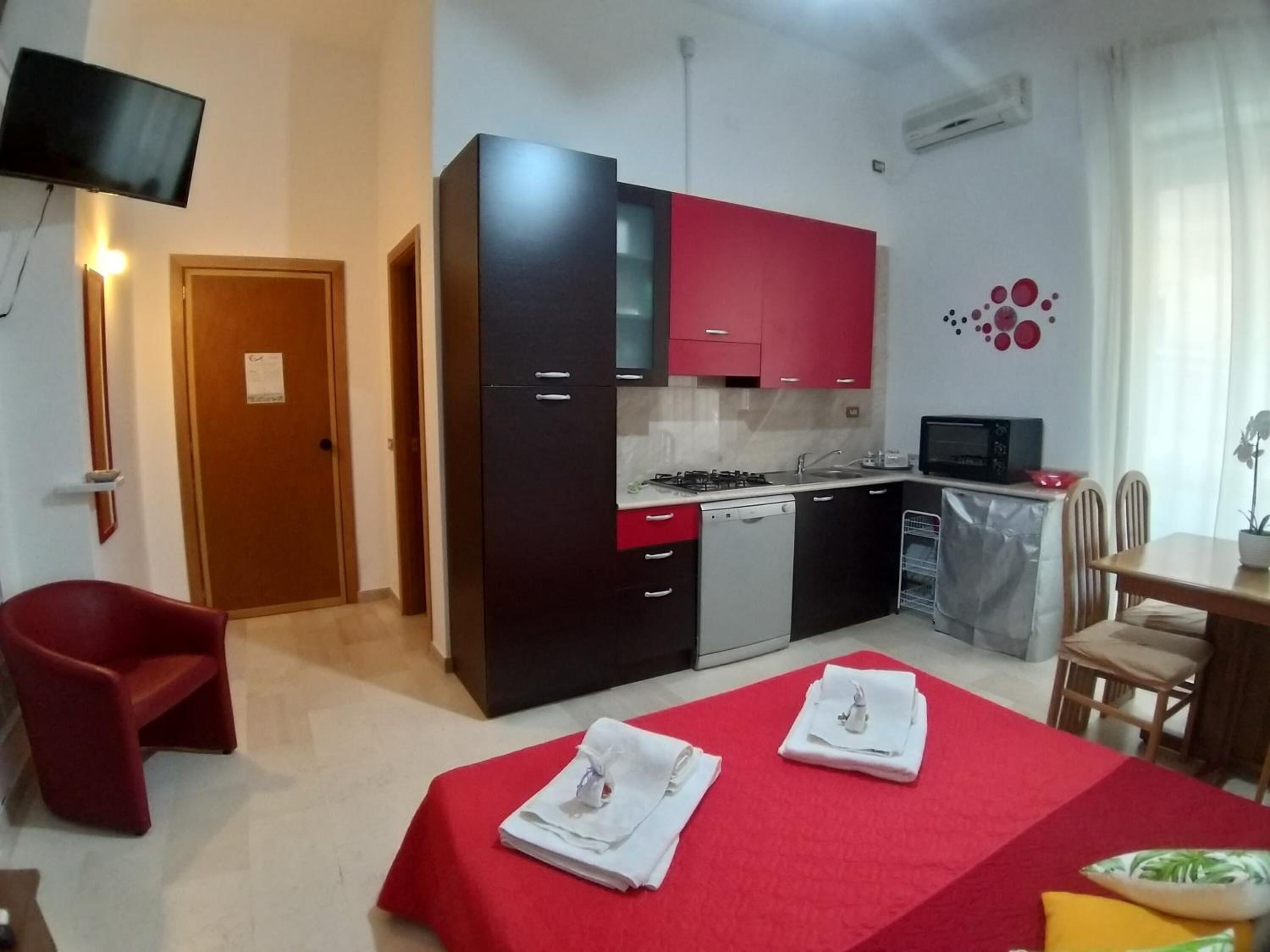 A compact kitchen with modern appliances, a dining area with a table and chairs, and a TV mounted on the wall.
