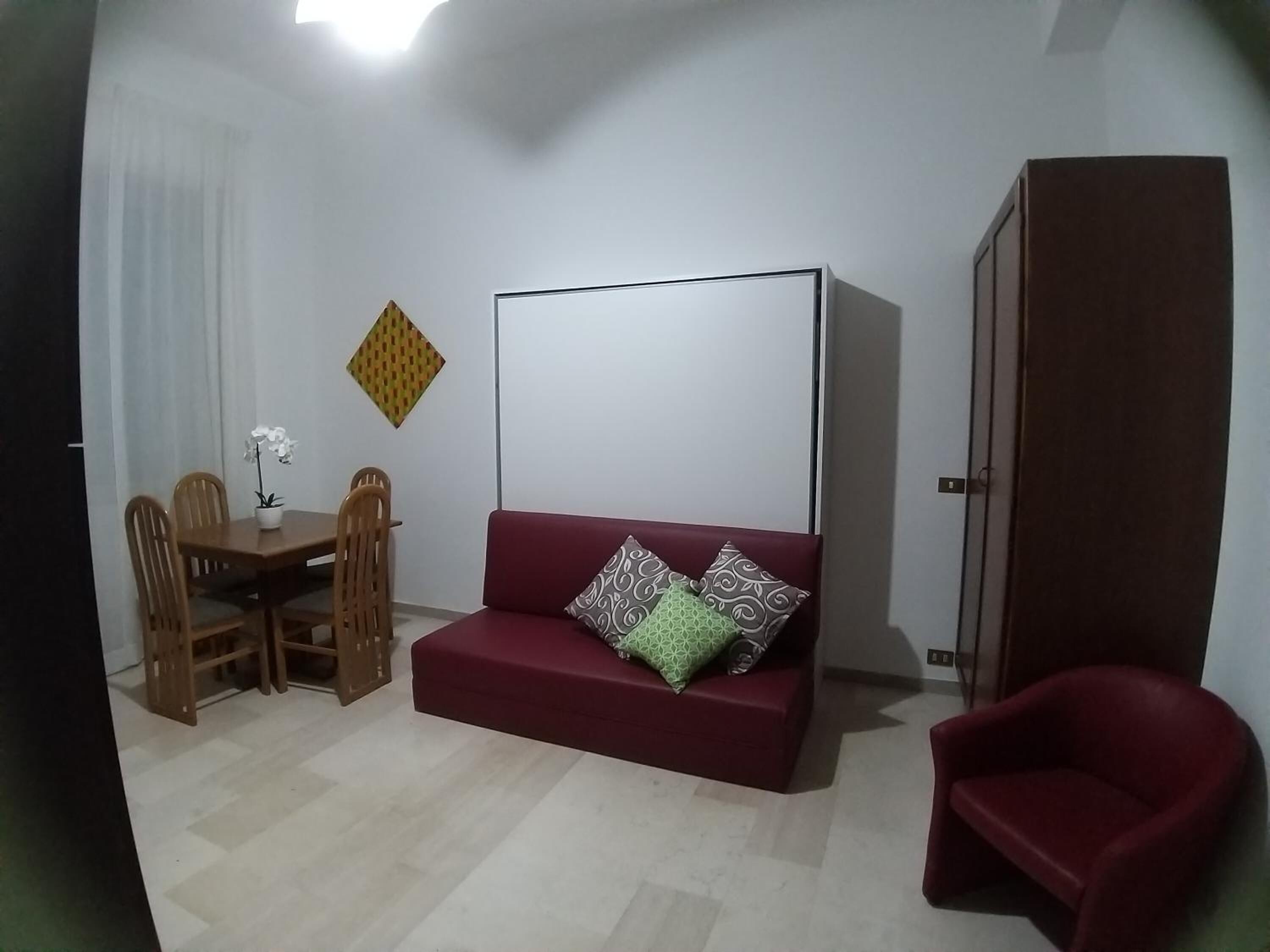 Ein Wohnzimmer mit einem roten Sofa, einem Holzespeisetisch mit Stühlen, einem kleinen Topfpflanzen und einem Kleiderschrank.
