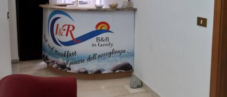 Ein Zimmer mit einer roten Couch, einem Fenster mit weißen Vorhängen, einer Theke mit einem Logo und dekorativen Tellern an der Wand.
