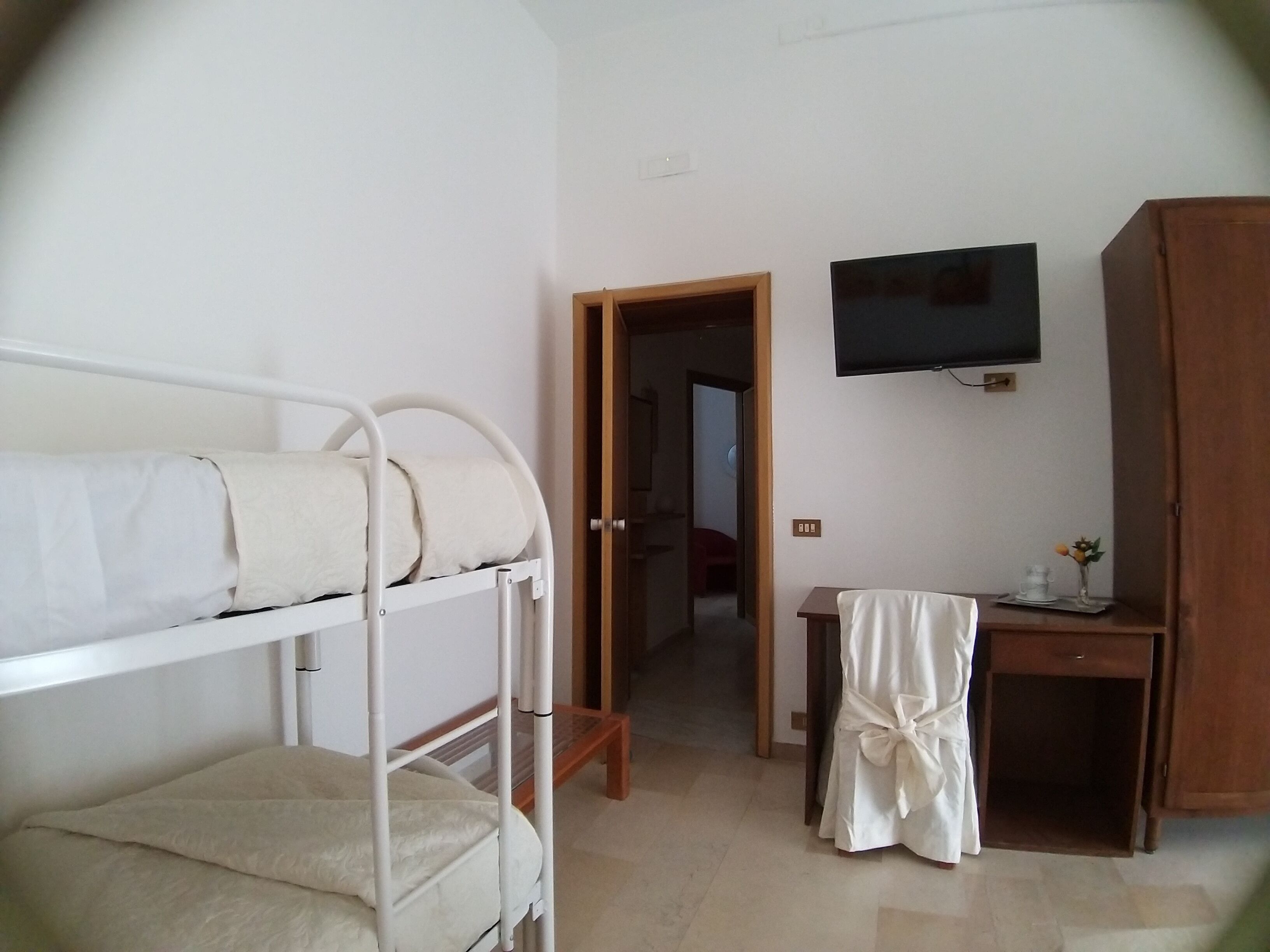 Una habitación con literas, un televisor montado en la pared, un armario de madera y una mesita con un jarrón.