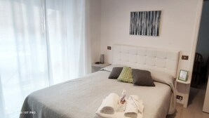 Habitación de hotel con cama, mesita de noche, una obra de arte colgada en la pared y una puerta que da a otra habitación.