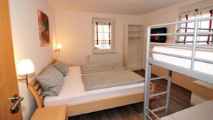 A compact room with a bunk bed, a bedside table, a lamp, a window with blinds, and a door. - Ferienwohnungen am Sonnenplatz (Rust)