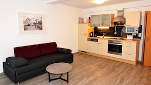 A modern kitchen with a gas stove, microwave, and oven. There is a dark sofa with red cushions and a small round table. A framed picture hangs on the wall. - Ferienwohnungen am Sonnenplatz (Rust)