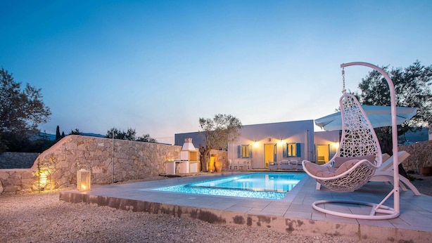 Una piscina con una sedia a dondolo, un muro in pietra e illuminazione esterna.