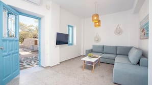 Un soggiorno con una porta blu, una TV a schermo piatto, un divano grigio, un tavolino e una lampada a sospensione.
