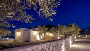 Un muro di pietra, un vialetto lastricato e un edificio con finestre illuminate di notte.
