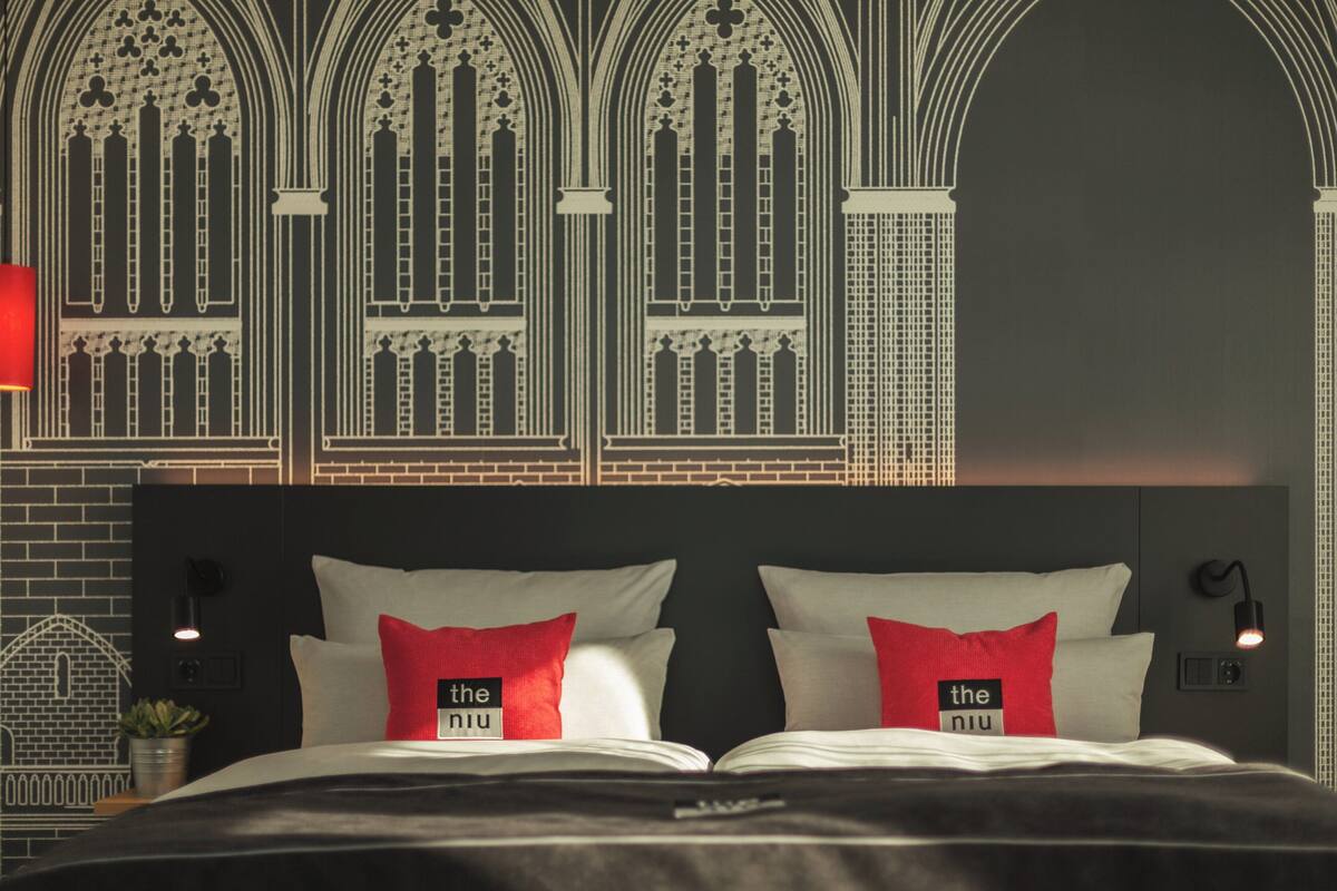 Une chambre d’hôtel avec un grand lit, deux oreillers rouges et un mur agrémenté de fenêtres en arc de cercle.