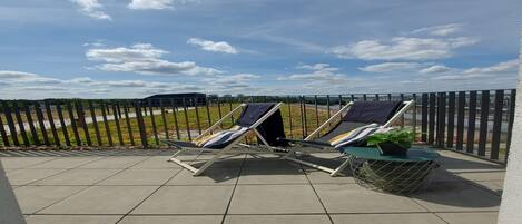 A terrace with two lounge chairs, a small table, and a potted plant.