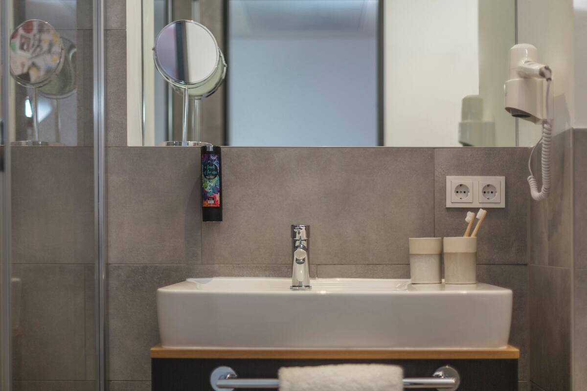 Une salle de bain moderne avec un lavabo blanc, un miroir, un sèche-cheveux et un porte-serviettes.