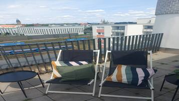A balcony with two chairs and a small table, overlooking a railway track and buildings.