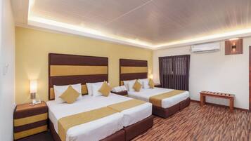 A hotel room with two beds, a wooden bench, a nightstand with a phone, and an air conditioning unit on the wall.