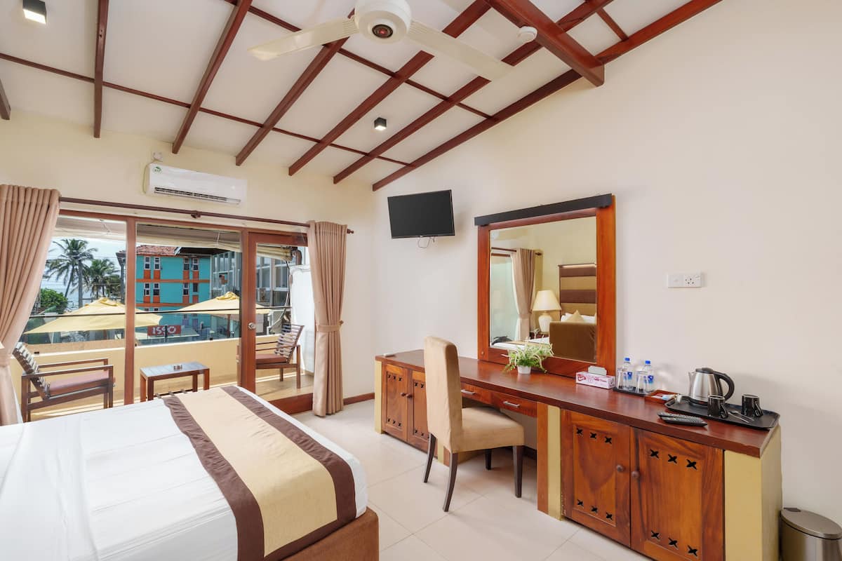 Habitación de hotel con cama, escritorio, silla y un espejo grande. Hay un televisor en la pared y una ventana con cortinas.