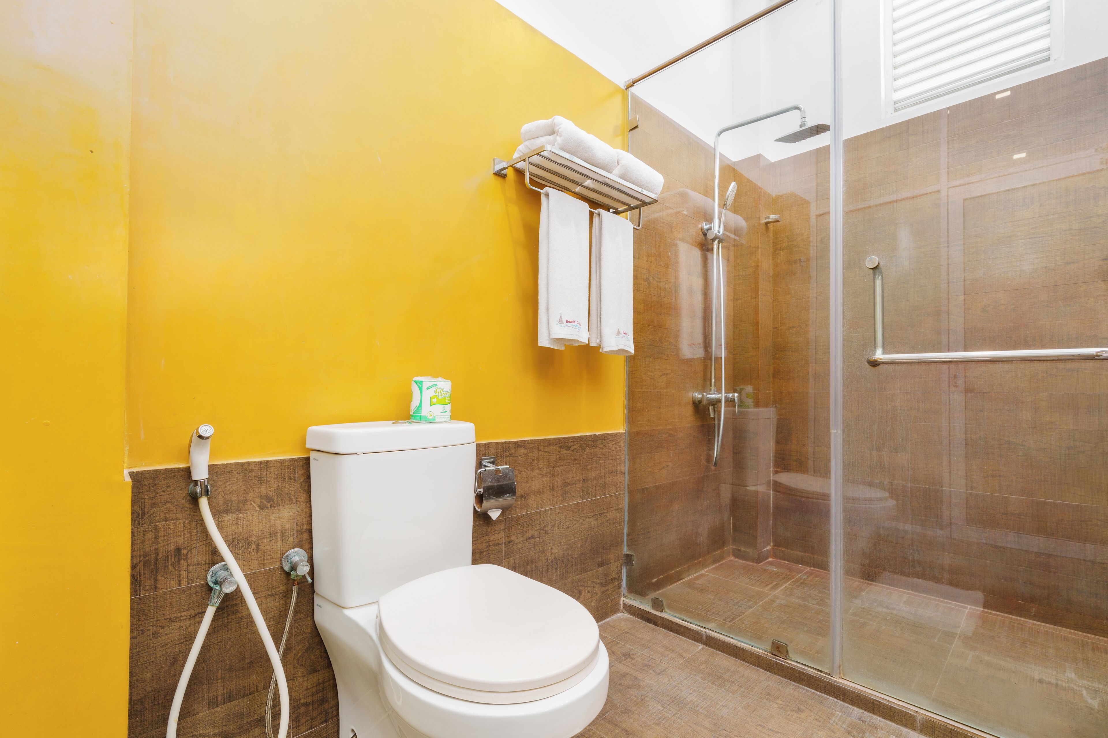 A bathroom with a yellow wall, a white toilet, a glass shower enclosure, and a towel rack with two towels.