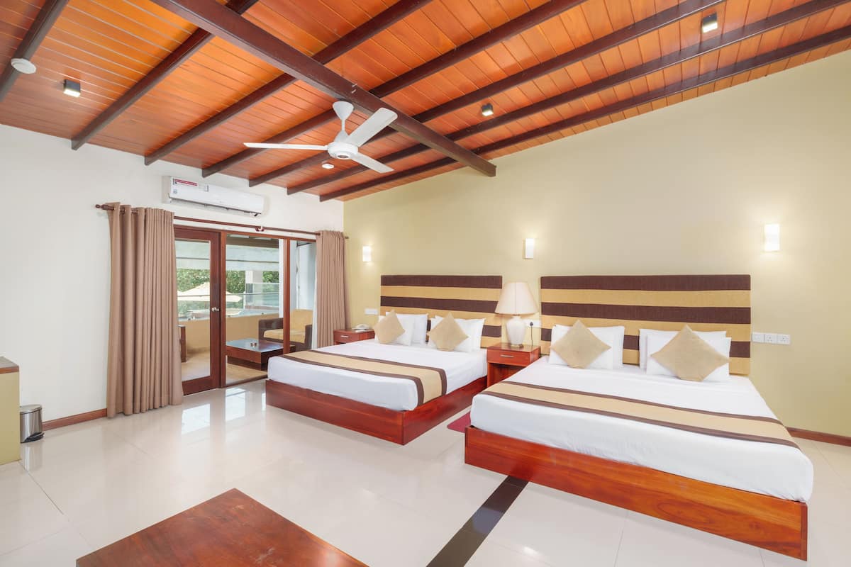 Habitación de hotel con dos camas, vigas de madera en el techo, ventilador de techo, equipo de aire acondicionado y vista al exterior a través de un ventanal.